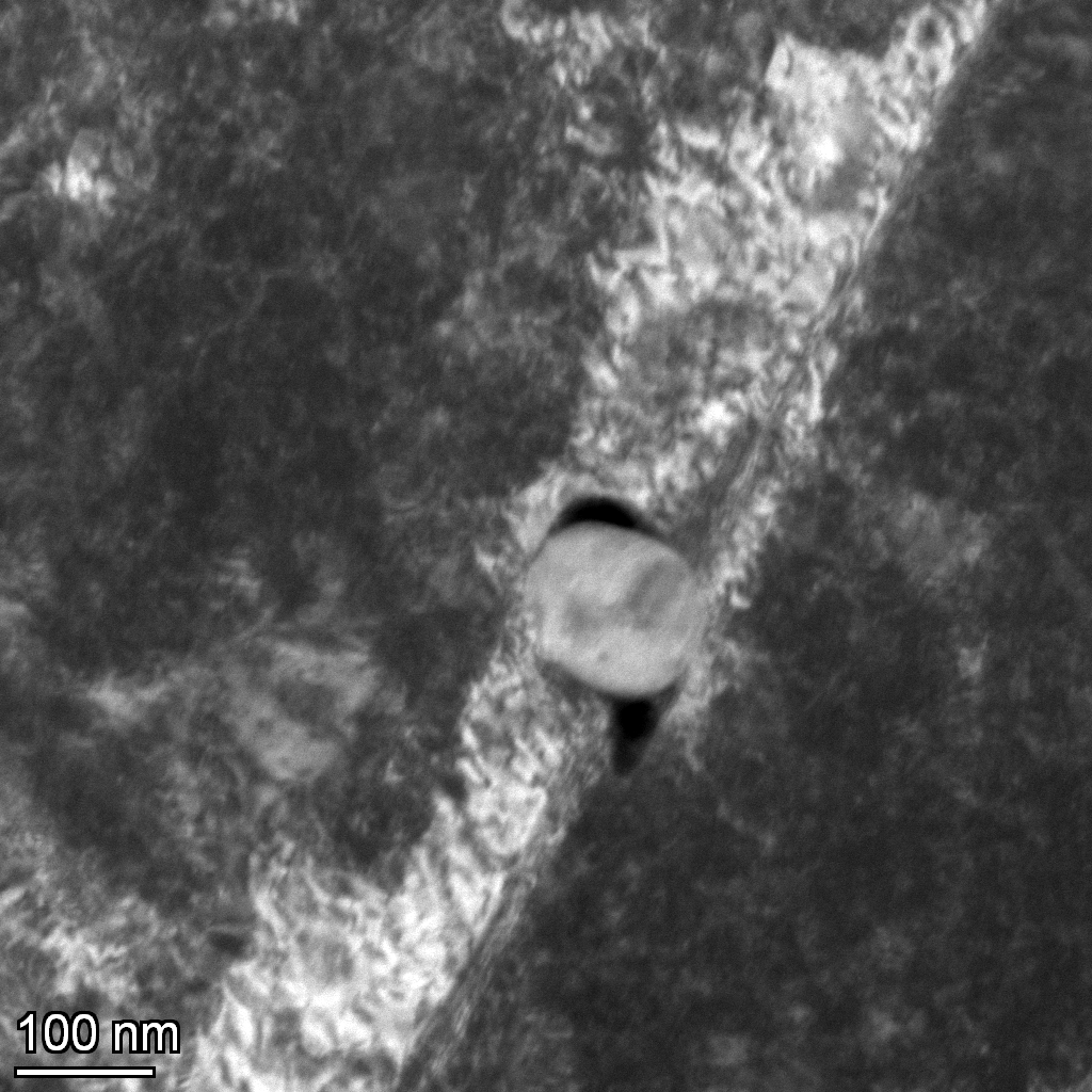 TEM image of a nanoparticle in a metal matrix showing void elongation along the tensile axis and twin planes confined around the nanoparticle.